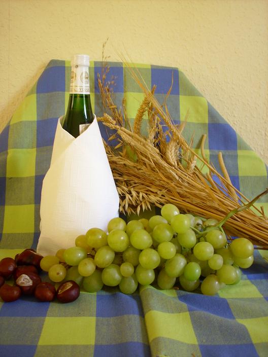Herbstdekoration bestehend aus Kastanien, Weintrauben, Getreide und einer Flasche Federweißer.